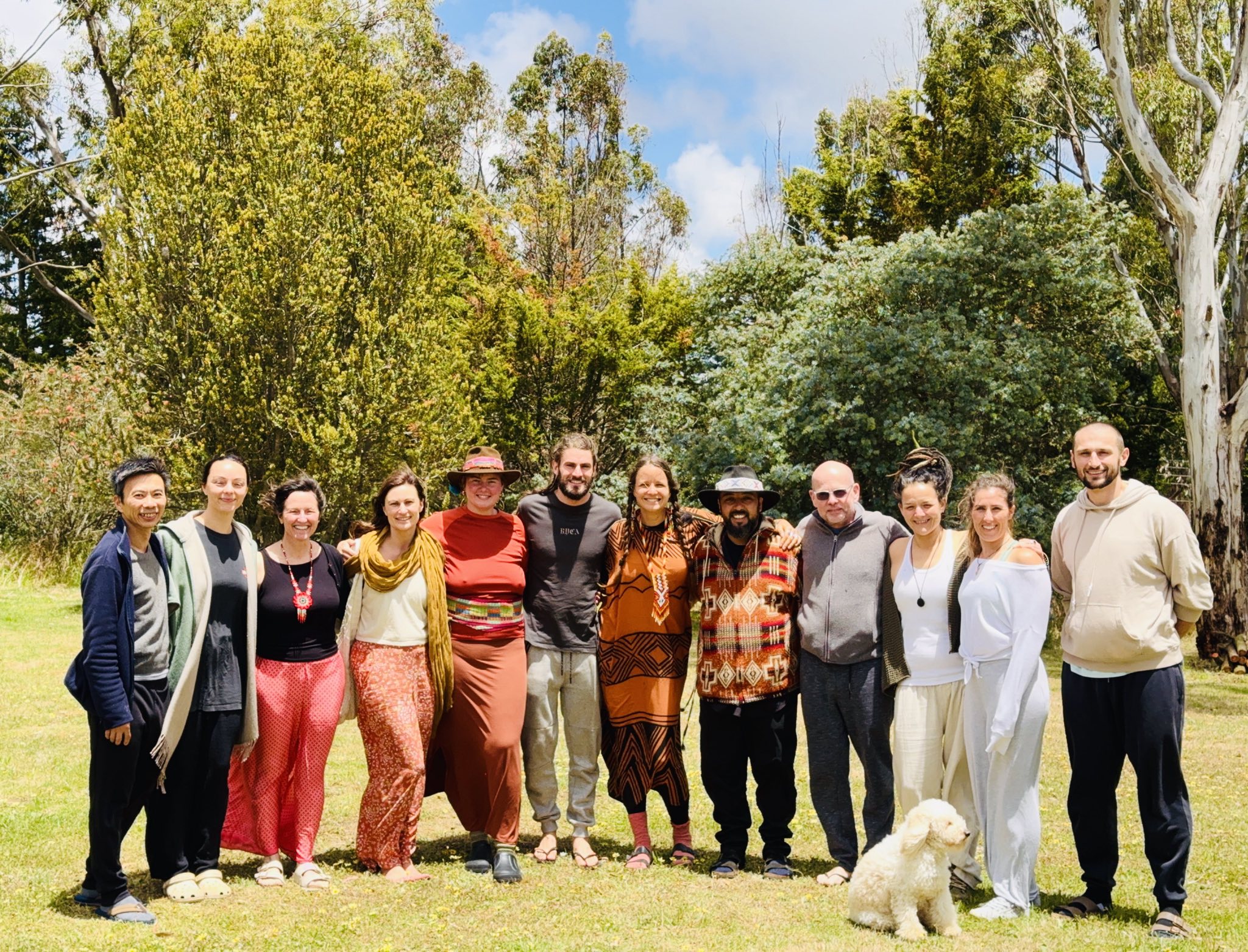 A group standing together in a sunlit garden, with trees behind them and a small dog in front.
